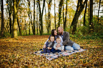 Fototapeta premium Happy caucasian family of mom dad and little girl with boy sitting on plaid at majestic autumn fall forest.