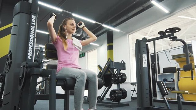 Sporty caucasian girl, in pink t-shirt and grey tracksuit bottoms, using towel during workout at the gym
