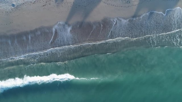 Waves washing ashore sandy beach, top down aerial descent.