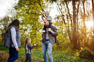 Naklejka na ściany i meble Happy caucasian family of mom dad and little girl with boy at majestic autumn fall forest.