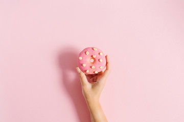 Women's hand holding donut on pink background. Minimal flat lay.