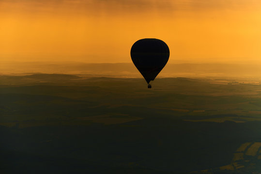 Aerial view of summer countryside during sunset with silhouette of hot air balloon