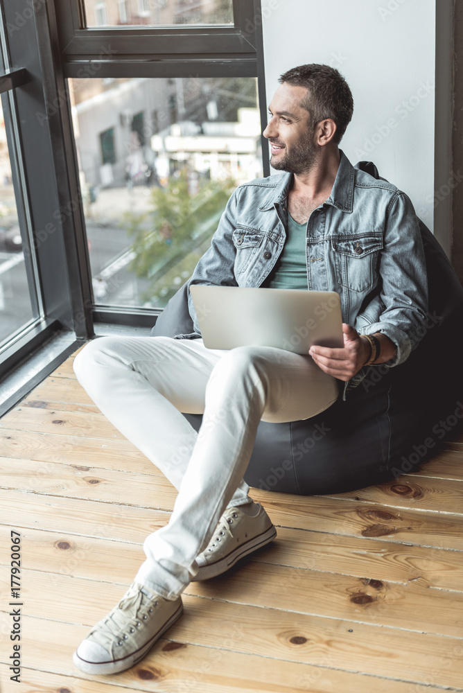 Wall mural positive cute man is working in cozy pillow near window