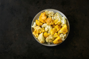 White and yellow cauliflower gratin served on gray ceramic plate over dark texture background. Flat lay with copy space. Restaurant menu concept.