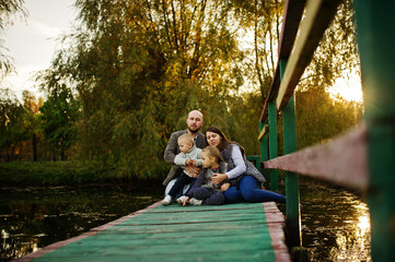 Happy caucasian family of mom dad and little girl with boy at wooden pier on majestic autumn fall forest.