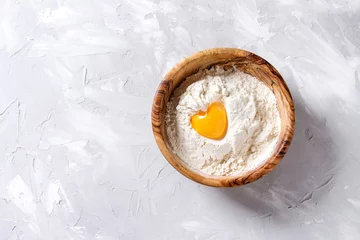  Olive wood bowl with wheat flour and whole egg yolk as heart shape over gray texture background. Top view with copy space. Baking concept © Natasha Breen