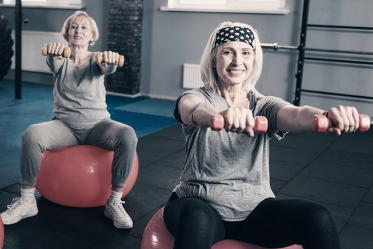 Two senior women stretching out hands with dumbbells