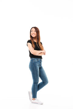 Full length photo of young pretty chinese woman in black tshirt and jeans standing with crossed hands, looking aside
