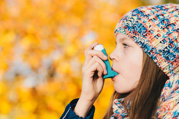 Asthma patient girl inhaling medication for treating shortness of breath and wheezing in a park - obrazy, fototapety, plakaty
