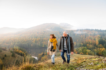 Senior couple on a walk in an autumn nature. - obrazy, fototapety, plakaty