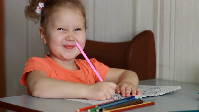 Very funny little girl draws with pencils, smiles and looks at the camera. The child is teasing