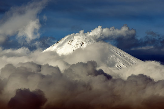 Volcanic landscape of Kamchatka Peninsula: top of cone of active Avacha Volcano, fumaroles activity of volcano - steam and gas plume from crater, clouds drifting across sky near volcano.