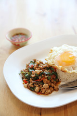 stir fried pork and basil with rice and egg on wood background thai food
