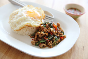 stir fried pork and basil with rice and egg on wood background thai food