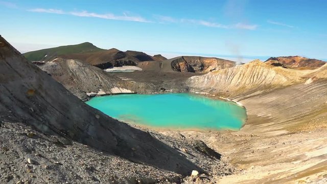 Panorama of the slope of Ebeko volcano on Paramushir Island. Acid lake in the crater of the volcano and the top of the mountain behind the strait covered by fog. Kuril Islands, Russia
