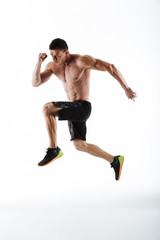 Full length photo of young powerful sports man jumping over white background