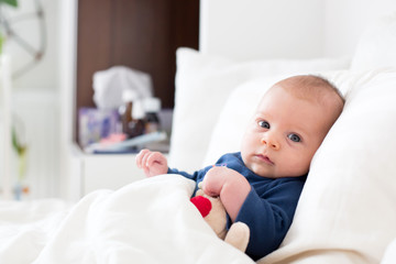 Cute newborn baby boy, lying in bed with cold