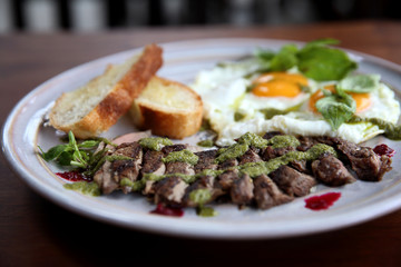 Grilled beef steak with toast , fried egg and vegetables on top with pesto sauce