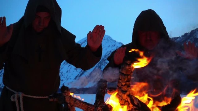 Two monks pray at the campfire in the mountains slow motion
