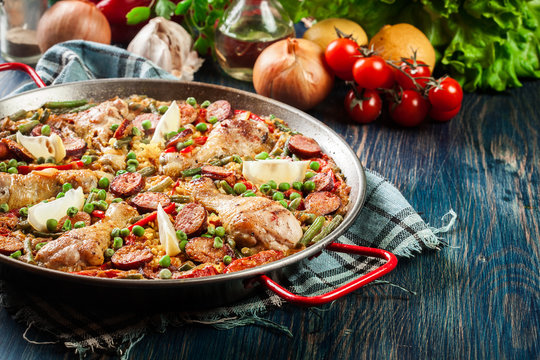 Traditional paella with chicken legs, sausage chorizo and vegetables served in paellera