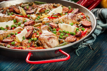 Traditional paella with chicken legs, sausage chorizo and vegetables served in paellera