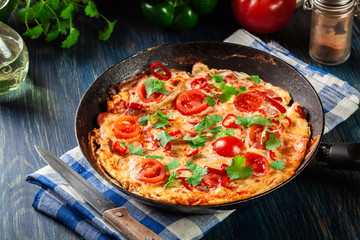 Frittata made of eggs, sausage chorizo, red pepper, green pepper, tomatoes, cheese and chili in a pan on wooden table