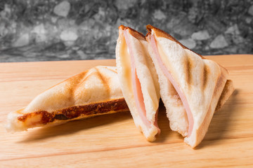 Bread toast made to sandwich with ham and cheese on wood plate.