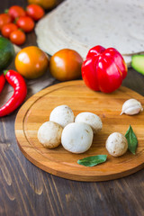 White mushrooms surrounded by vegetables on kitchen board.