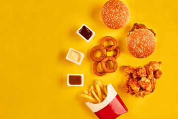 Obraz na płótnie Canvas Top view hamburger, french fries and fried chicken on yellow background. Copy space for your text.