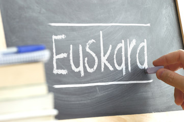 Hand writing on a blackboard in a language class with the word BASQUE wrote on. Some books and...