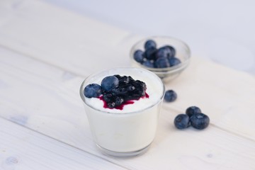 Glass cup of yogurt with blueberries on white table and white background