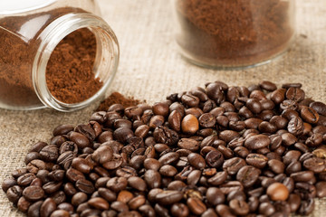 Roasted coffee beans and glass jar with ground coffee inside, closeup