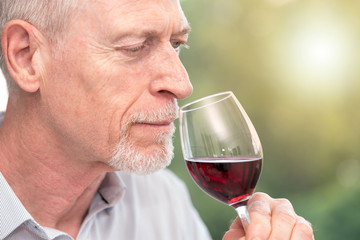 Mature man tasting red wine, light effect