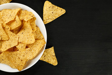 Corn chips nachos in a white plate on a black background top view, text space