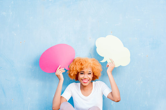 Beautiful african woman holding colorful thoughtful bubbles on the blue wall background