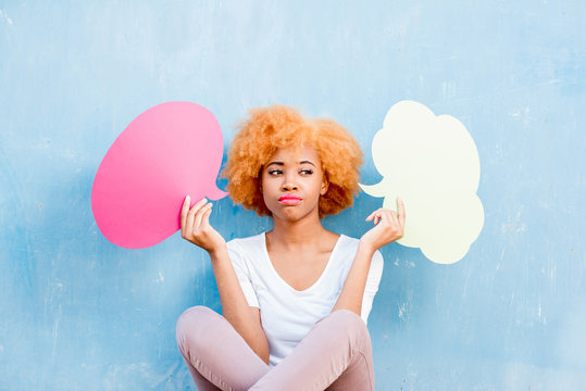 Beautiful african woman holding colorful thoughtful bubbles on the blue wall background
