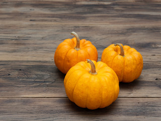 Three orange pumpkins in big, medium, and small size on dark wooden background show colorful pattern and scale used in Halloween, still life, kitchen, and comparison, and country themes