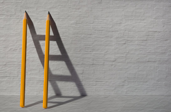 Two pencils and a shadow in form of ladder near the stone wall. Success, teamwork and solving problems business concept. Copy space for text .