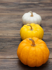 Small white, medium yellow, and big orange pumpkins put vertically on dark wooden background show colorful pattern and scale used in Halloween, still life, kitchen, and comparison, and country themes