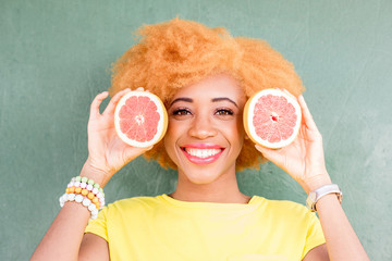 Portrait of a beautiful african woman with grapefruit slices on the green wall background