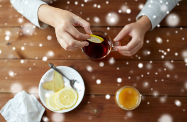 close up of ill woman adding lemon to tea cup