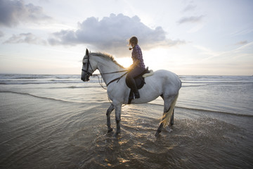 Women horse riding on beach at sunset.