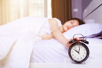 woman sleeping on bed and rise hand to turn off alarm clock in bedroom