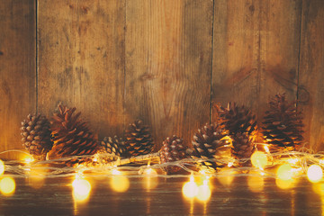 Holiday image with Christmas golden garland lights and pine cones over wooden background