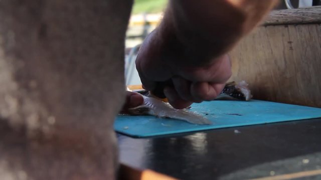 Mann filetiert drau&szlig;en Fisch (Dorsch) auf Schneidebrett mit Filetiermesser auf Boot kurz nach dem Fang bei Sonne
