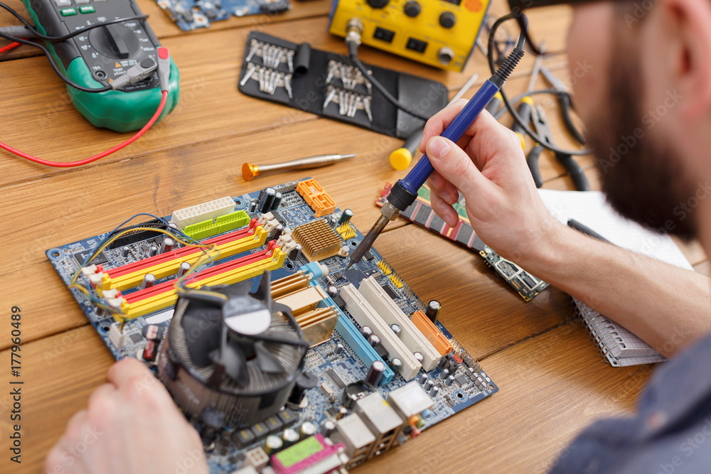 Poster repairman soldering computer circuit in workshop