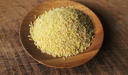 Dry bulgur wheat in wooden bowl isolated Spilled bulgur