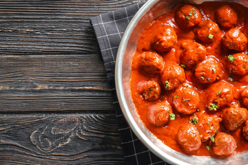 Saucepan with delicious meatballs in tomato sauce on table