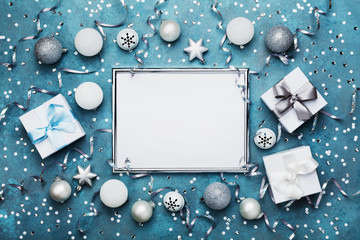 Magic christmas background. Frame with xmas decoration, gift box, confetti and silver sequins on vintage blue table top view. Flat lay. Party mockup or festive invitation.