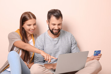 Young couple with laptop and credit card on color background. Internet shopping concept